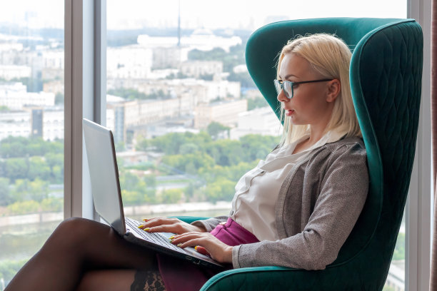 一个女人坐在扶手椅上，手里拿着笔记本电脑图片下载