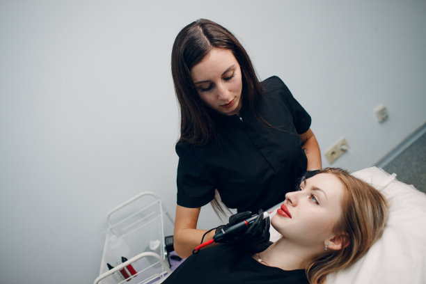 美容师在年轻女子的嘴唇上画上红色的永久彩妆纹身图片下载