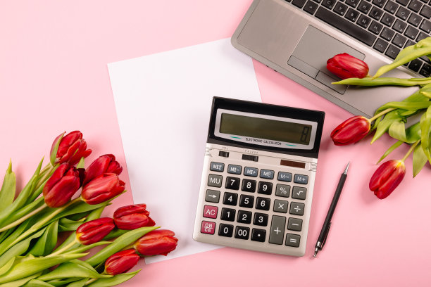 粉红色背景上的红色郁金香，配上计算器、笔记本电脑、笔记本、纸和笔，这些都是广告或博客可视化的模板，为文字留出自由空间。假日商务领域图片下载