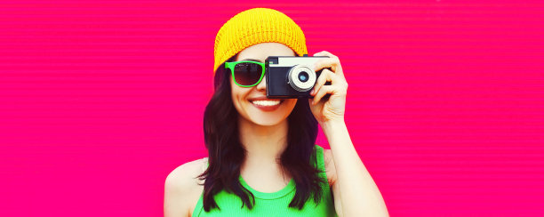 夏天快乐微笑的年轻女子摄影师的彩色肖像与粉红色背景相机拍照，空白的广告文字复制空间图片下载
