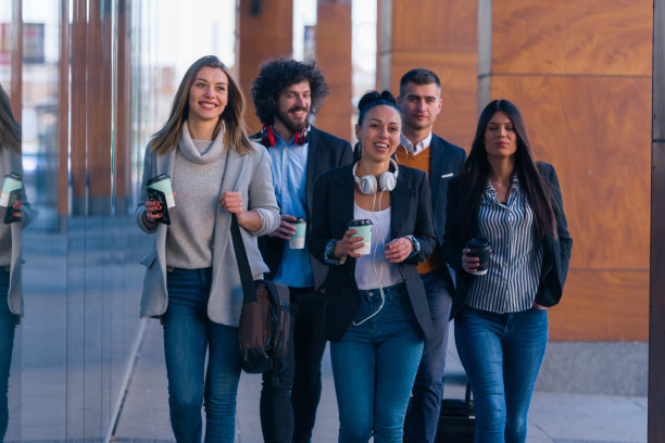 一群穿着休闲商务装的同事在办公室大厅里边走边讨论业务的全身照图片下载