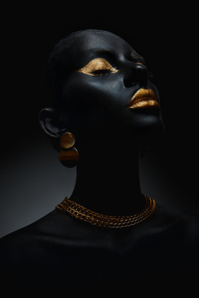 画着黑色皮肤彩绘的美女身体艺术，金链在他的手上和脖子上。金色的唇妆眼睑，金色的指甲涂在指尖上。专业化妆图片下载