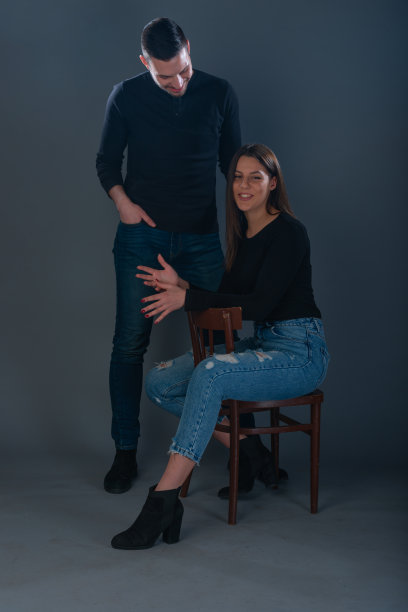美丽的女人坐在椅子上，英俊的男人站在她旁边的黑暗背景的工作室图片下载