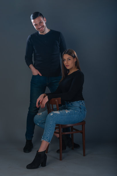 美丽的女人坐在椅子上，英俊的男人站在她旁边的黑暗背景的工作室图片下载