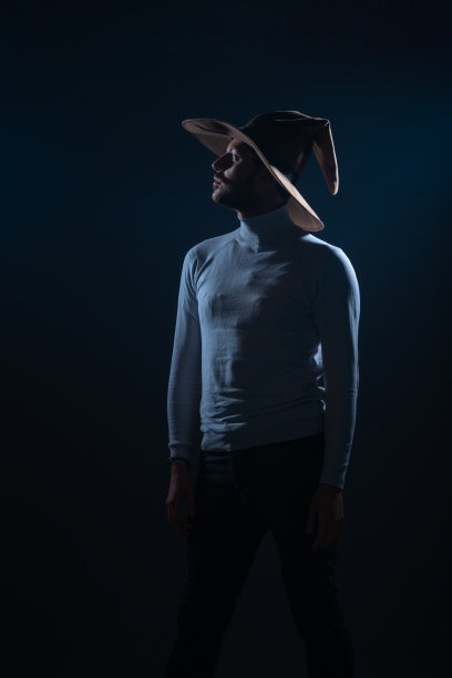 一个性感的年轻男子的肖像与牛仔帽摆姿势在高对比和黑暗的背景工作室图片下载