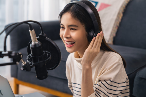年轻的亚洲女性使用麦克风，戴着耳机，用笔记本电脑录制播客。内容创造者的概念。图片下载