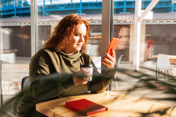 一个漂亮的胖女人看着手机的肖像。一个女人在咖啡店里休息，用着智能手机。社交网络的概念图片下载