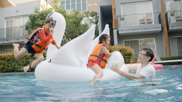 孩子们享受暑假。可爱的男孩和女孩穿着泳装和救生衣，从一个大橡胶圈上跳下来，和爸爸一起在游泳池里玩水。亚洲家庭在度假活动中快乐而有趣。图片下载