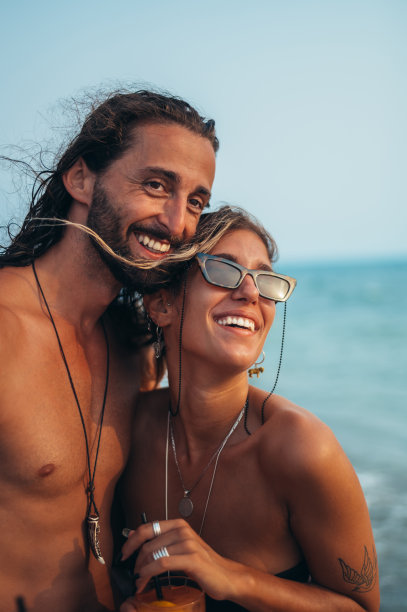 迷人的年轻夫妇带着酒精鸡尾酒在海滩上散步图片下载