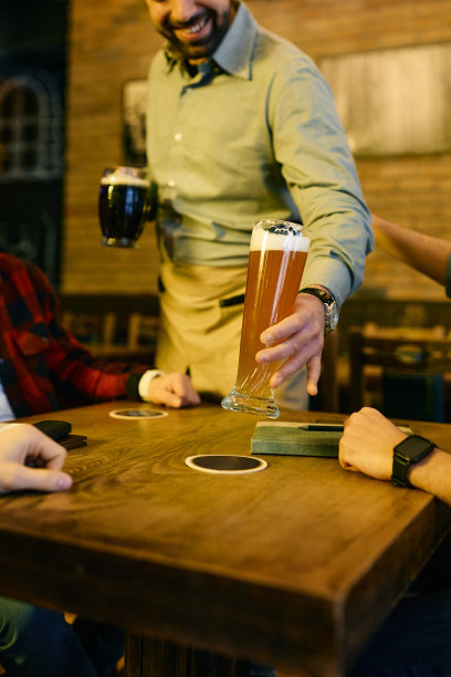 一个酒吧里侍者给一群男人端啤酒的特写镜头。图片下载