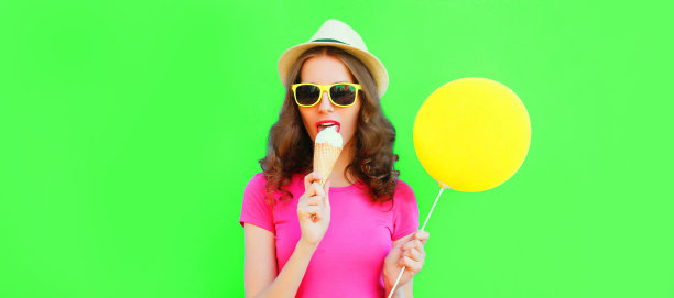 年轻女子的肖像与气球吃冰淇淋，戴着夏季草帽在绿色的背景图片下载