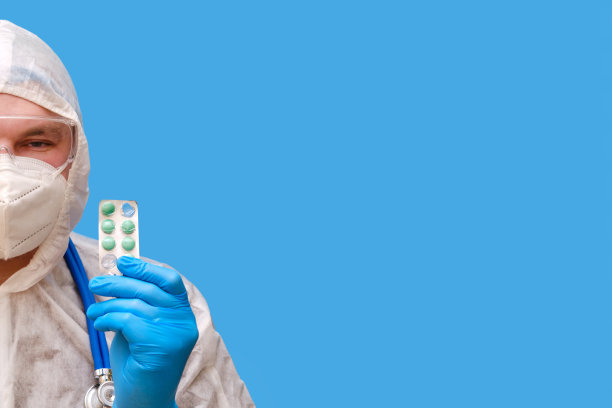 医生穿着防护服，戴着护目镜和医用面罩，背景是工作室的蓝色，复印空间图片下载