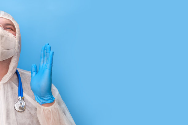 医生穿着防护服，戴着护目镜和医用面罩，背景是工作室的蓝色，复印空间图片下载