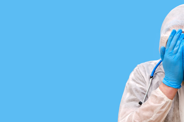 医生穿着防护服，戴着护目镜和医用面罩，背景是工作室的蓝色，复印空间图片下载