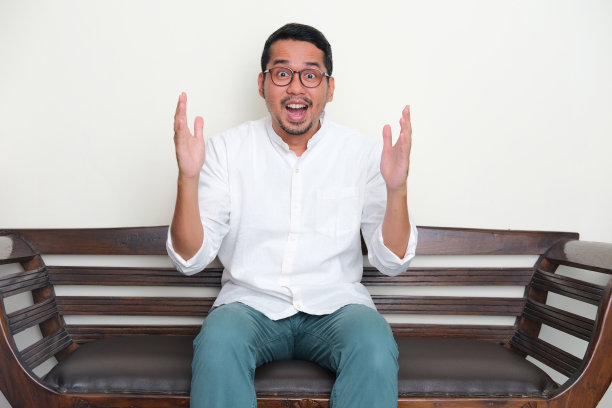 成年亚洲人坐在沙发上显示惊讶的表情图片下载