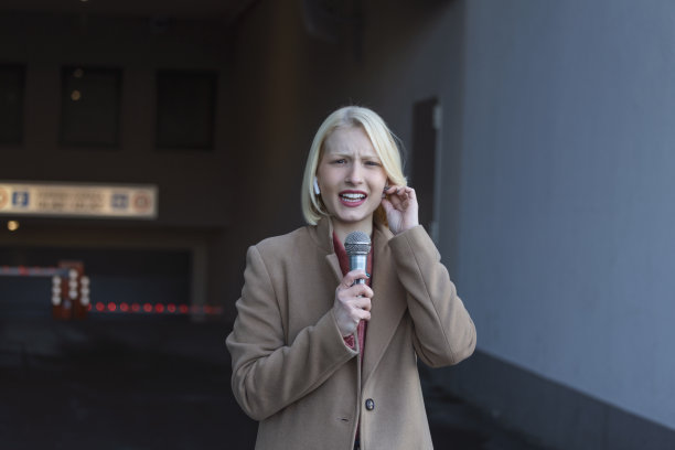 剪裁肖像的专业女记者在工作。年轻女子站在街上，手里拿着麦克风，对着镜头微笑。水平。选择性地关注女性图片下载