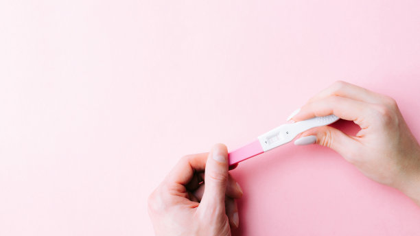 妊娠试验阳性。女性手握阳性怀孕测试与丝带粉红色背景。医疗保健妇科，孕产期产妇的观念。图片下载