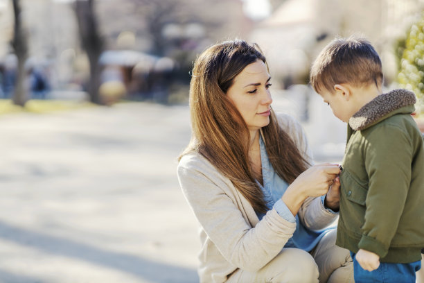 一位慈爱的母亲在公园里给一个小男孩拉夹克。图片下载
