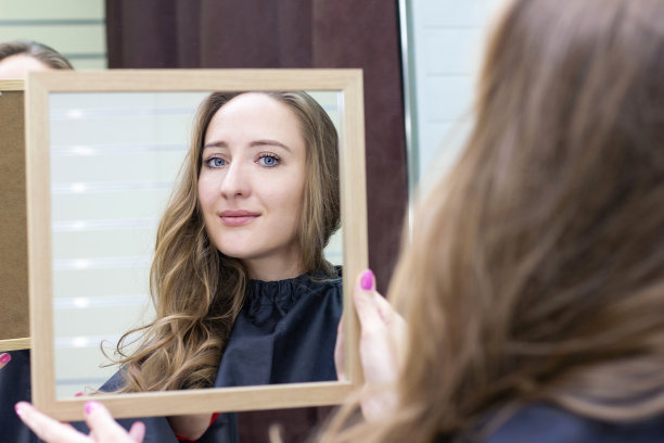 年轻漂亮的女人在美容院照镜子。化妆和发型图片下载