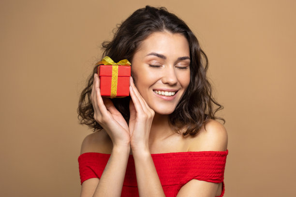 一位身穿红色上衣、米色背景的女士，手里拿着一份礼物，面带微笑。一个生日惊喜图片下载