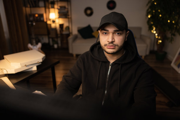 一个沉迷于电脑的人的肖像，在IT行业远程工作，信息学，程序员，黑客，网络犯罪，神秘的家伙穿着黑色运动衫，戴着棒球帽，黑暗的房间图片下载