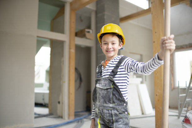 一个戴着黄色安全帽、穿着工装裤的酷男孩，在一所房子里，手里拿着铲子图片下载