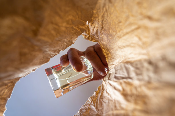 一只手把一瓶黄色的香水放在纸袋里。一个成熟男人的手把玻璃瓶放在打开的棕色袋子上。从下往上射击。关闭了。有选择性的重点。图片下载