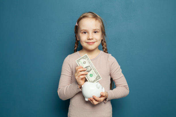 聪明快乐的小女孩，手里拿着扑满和一美元钞票图片下载