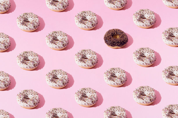 环形甜甜圈与白色和巧克力釉和小彩色碎屑在粉红色的柔和的背景。最小的概念和设计。模式。图片下载
