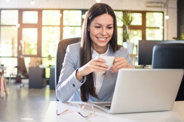 美丽的年轻女商人喝咖啡和在办公室使用笔记本电脑的肖像图片下载