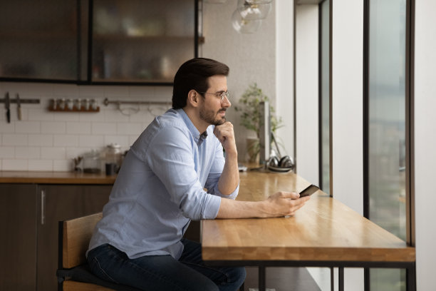 平静的商人坐在办公室厨房拿着智能手机做白日梦图片下载