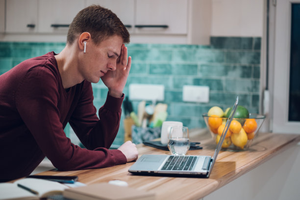 一个疲惫的红发男人在家工作时使用笔记本电脑图片下载