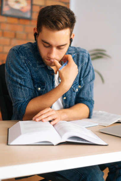 垂直肖像专注思考的年轻人阅读商业纸书坐在书桌与笔记本电脑在家里的办公室。图片下载