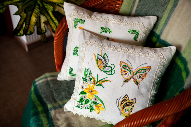 两个绣花的花朵和蝴蝶形状的枕头，放在一张盖着毯子的柳条椅上。舒适房间的内部图片下载