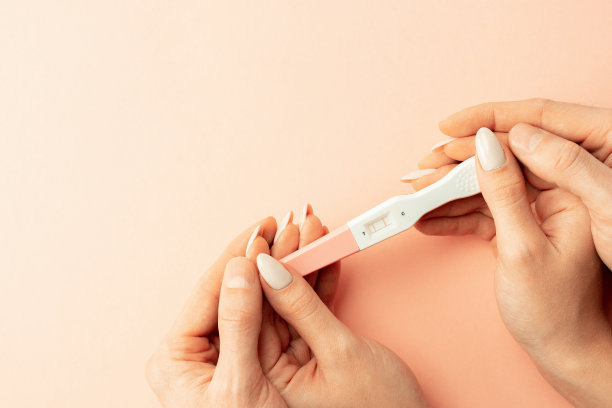 根验孕棒。女性手握阳性怀孕测试与丝带粉红色背景。医疗保健妇科，孕产期产妇的观念。图片下载