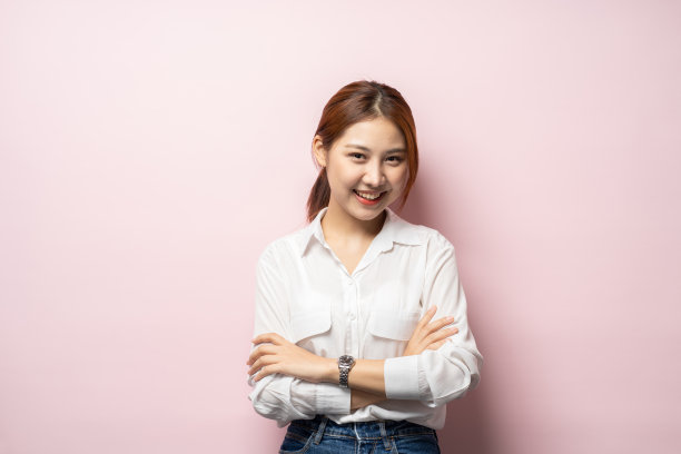 一个微笑的亚洲女商人站着双臂交叉的肖像，看着相机孤立在粉红色的背景。图片下载
