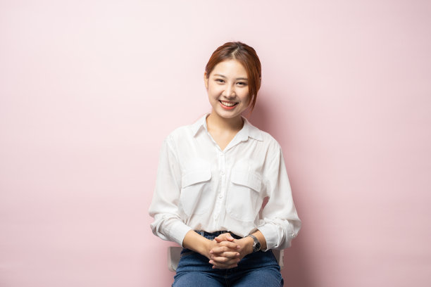 美丽微笑的女人看起来友好，准备帮助客户或客户，手牵手，盯着相机，粉红色的背景。图片下载