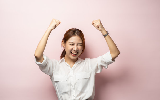 是的，我是赢家。成功的年轻女性实现目标或奖品，高举双手，欢呼着喜悦和兴奋，胜利和胜利像冠军，粉红色的背景。图片下载