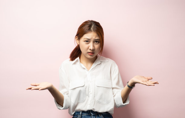 哦，对不起，我弄错了。女人耸耸肩，尴尬地笑着，感觉内疚，道歉，害羞地看着镜头，站在粉红色的背景上。图片下载