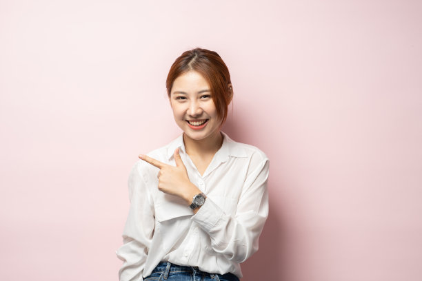 特写的欢快偷拍的女人斜着头可爱的指着左边，显示标志或广告，穿着白衬衫。图片下载