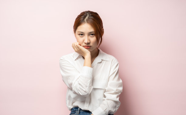 忧郁的年轻悲伤的亚洲金发女孩叹息不安的弯腰从额头下看孤独的不快乐的瘦手掌无聊的感觉后悔悲伤的忧郁的表情站粉红色的背景悲观。图片下载