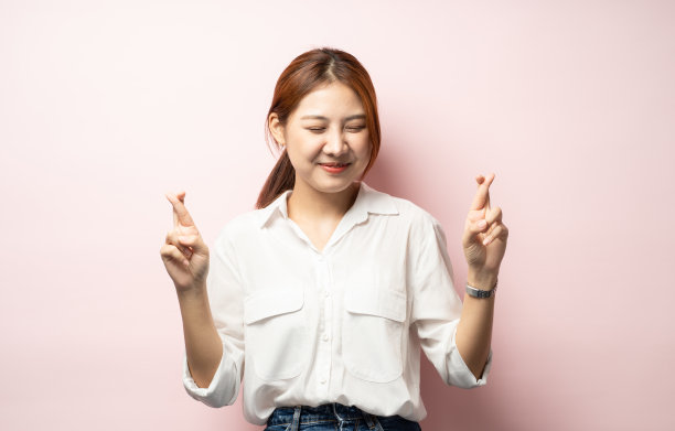 快乐的亚洲女孩笑着许愿，交叉手指乐观，祈祷好运，希望通过考试，期待大新闻，粉色背景图片下载