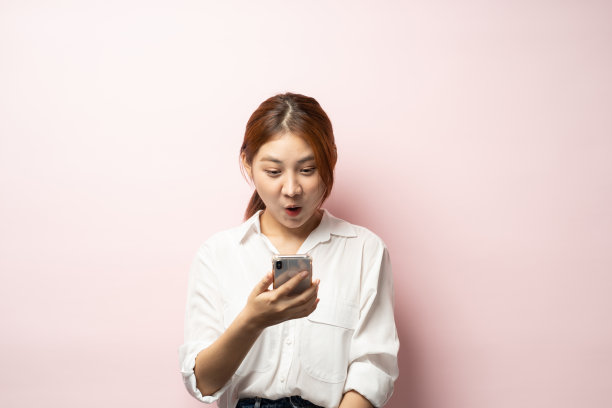 沮丧的亚洲妇女抱怨智能手机，拿着手机，看起来困惑，粉红色的背景。图片下载