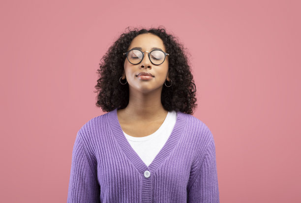 平静的年轻黑人女子戴着眼镜，闭上眼睛，在粉红色的画室背景下自由地呼吸图片下载