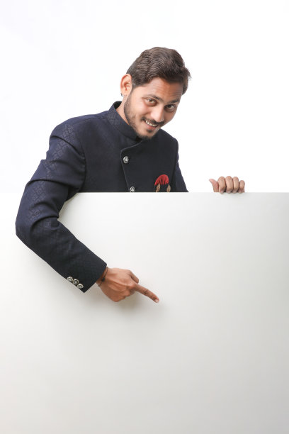 印度男子手持白板，在节日期间穿着传统服装，站在白色背景上推销商品。图片下载