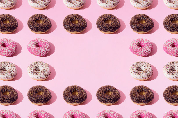白色、粉色和巧克力色的环形甜甜圈。粉红色粉彩背景上的彩色碎屑。模式。平的。副本的空间。图片下载