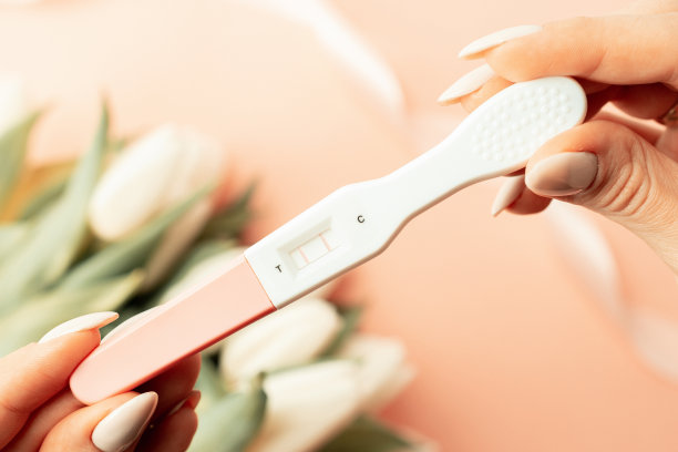 怀孕测试。阳性孕妇手中拿着粉红色的丝带，在郁金香花粉红色的背景上。新的生活和新的家庭。母性、怀孕、节育概念。图片下载