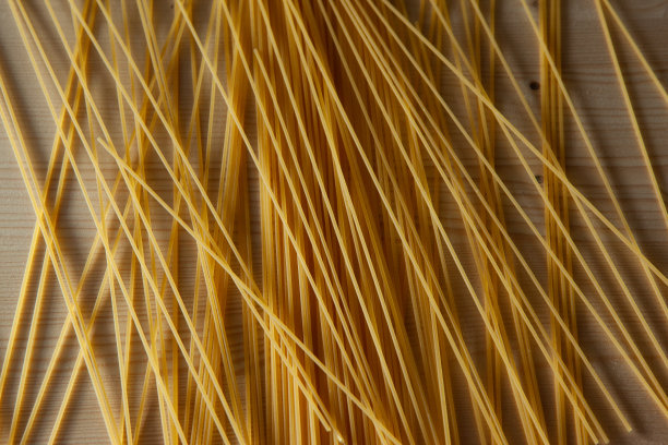 黄色的意大利面散落在桌子上。意大利食品的概念。意大利面条艺术背景的设计或项目，为出版物，海报，日历，壁纸，明信片，横幅，封面，网站图片下载