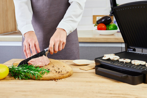 电烤架上的准备工作。穿着白衬衫和围裙的女人站在厨房里切肉。电烤烧烤。图片下载