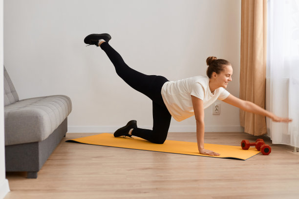 这张照片拍摄的是一名身穿白色t恤和黑色紧身裤的女运动员，她在家里做运动，做一条腿的平板支撑姿势，抬起手臂，锻炼臀部肌肉的灵活性。图片下载